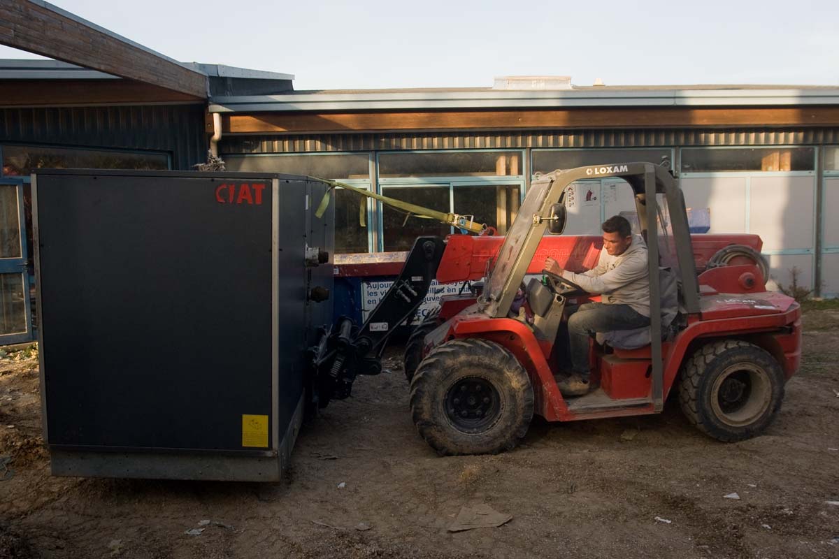 ouvrier sur un chantier déplacant un groupe froid à eau glacée à l'aide d'un chariot téléscopique